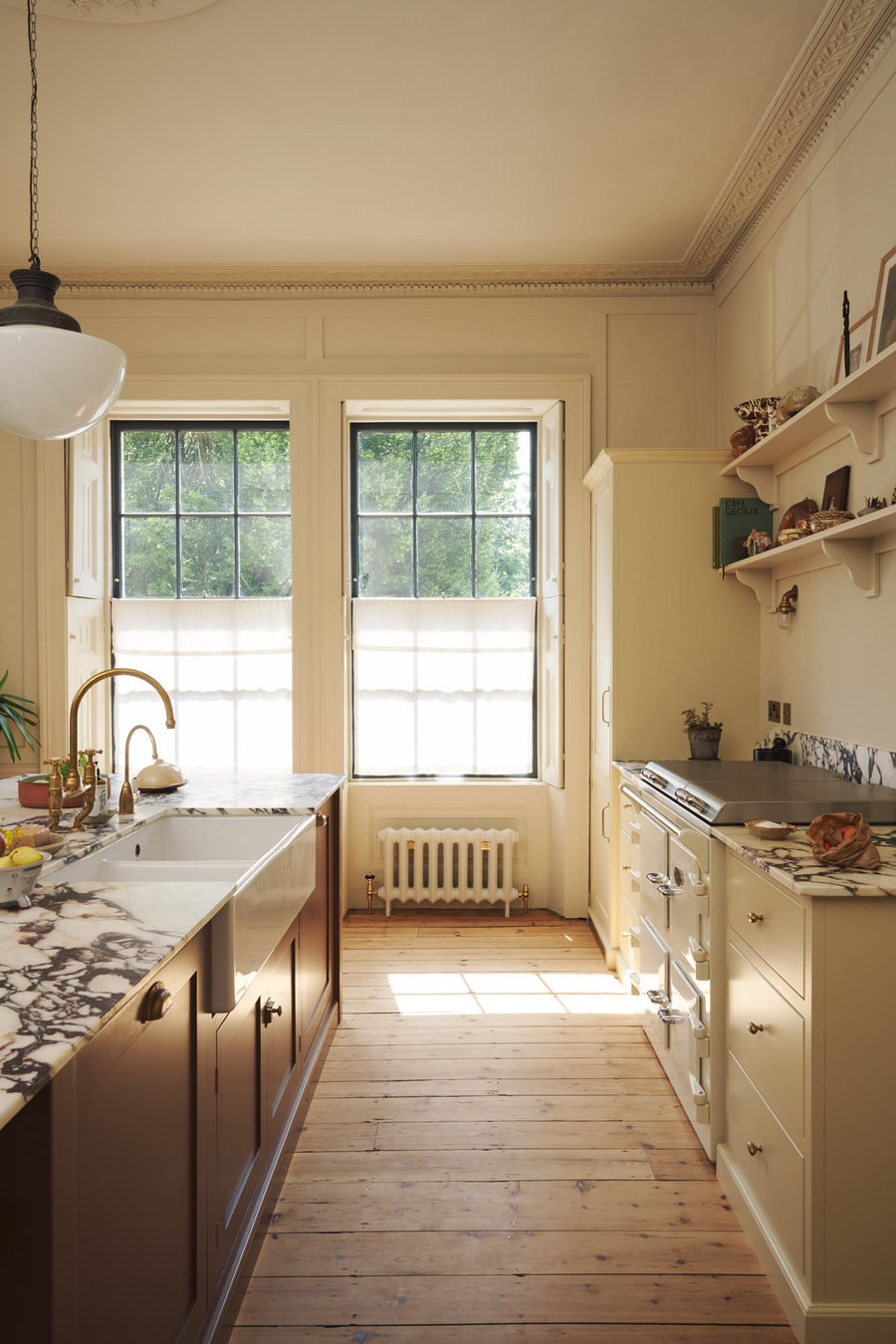 A bright, spacious, warm, and simple-yet-grand shaker kitchen featuring a large kitchen island with a Calacatta Viola worktop, a cooker run, a fridge/freezer cupboard, and long shaker shelves. Perfectly decorated with beloved vintage furniture and decor made from different natural materials, it crea