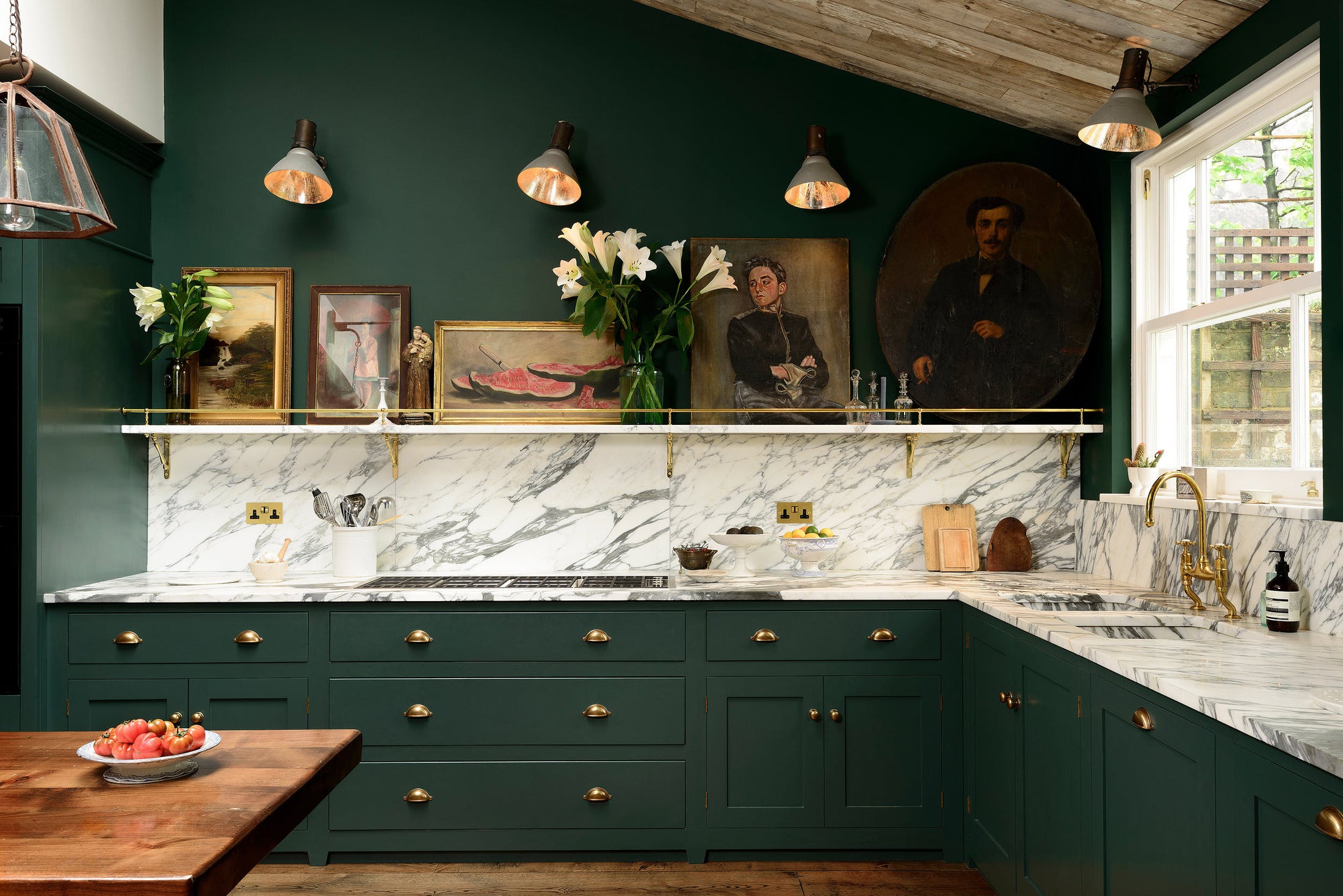 A lush green, classic English kitchen featuring an L-shaped sink and cooker, all complemented by Arabescato marble for the worktop, splashback, and countertop shelf. The kitchen includes full-height cabinets and a wall cupboard, creating a luxurious yet bohemian atmosphere. An angled wooden skylight